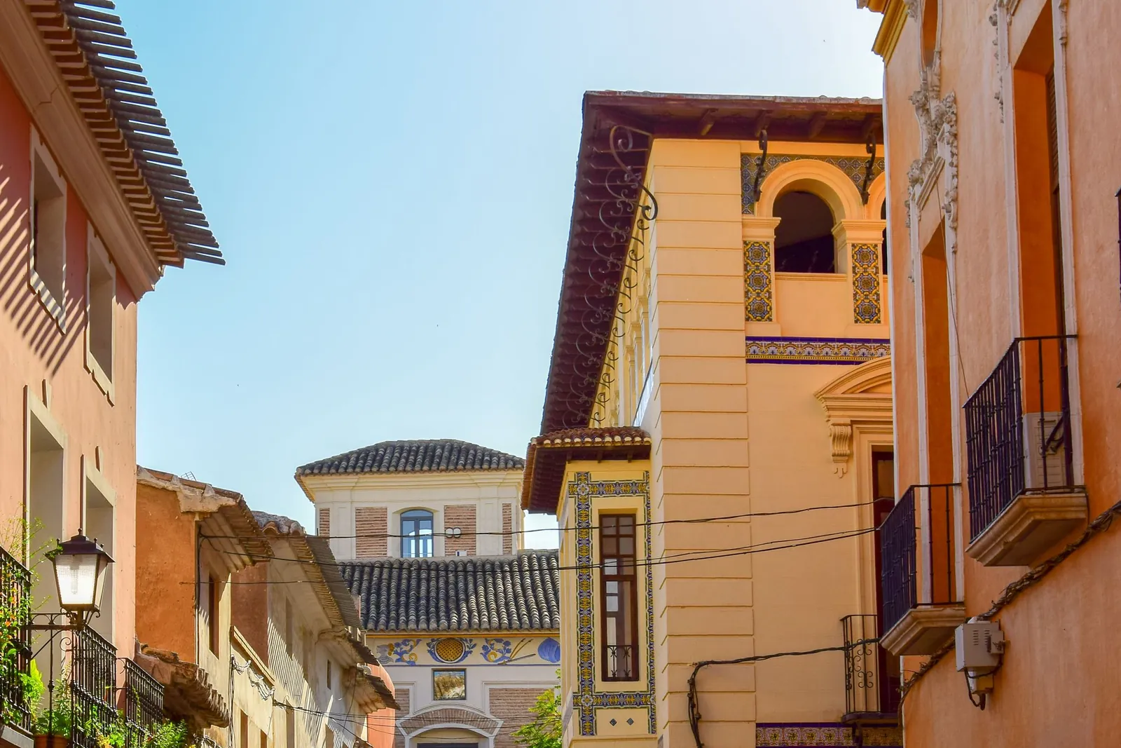 Calle del casco antiguo de Mula, en la Región de Murcia, con fachadas ocres, balcones de forja y frisos de azulejos